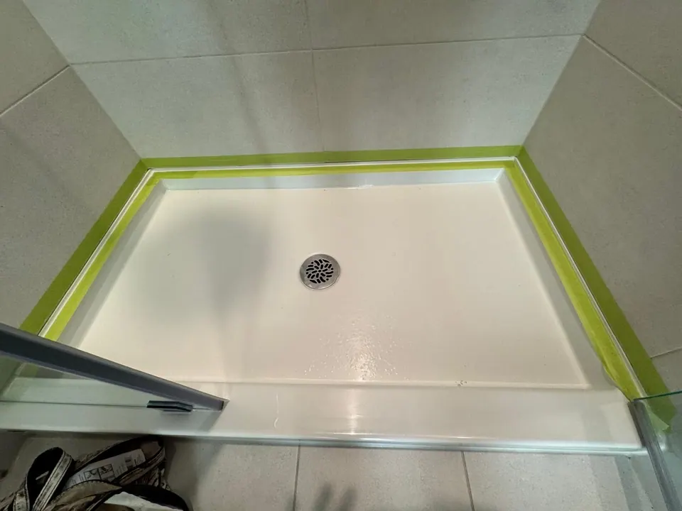 Before: Shower base edge masked with green tape, ready for new caulk