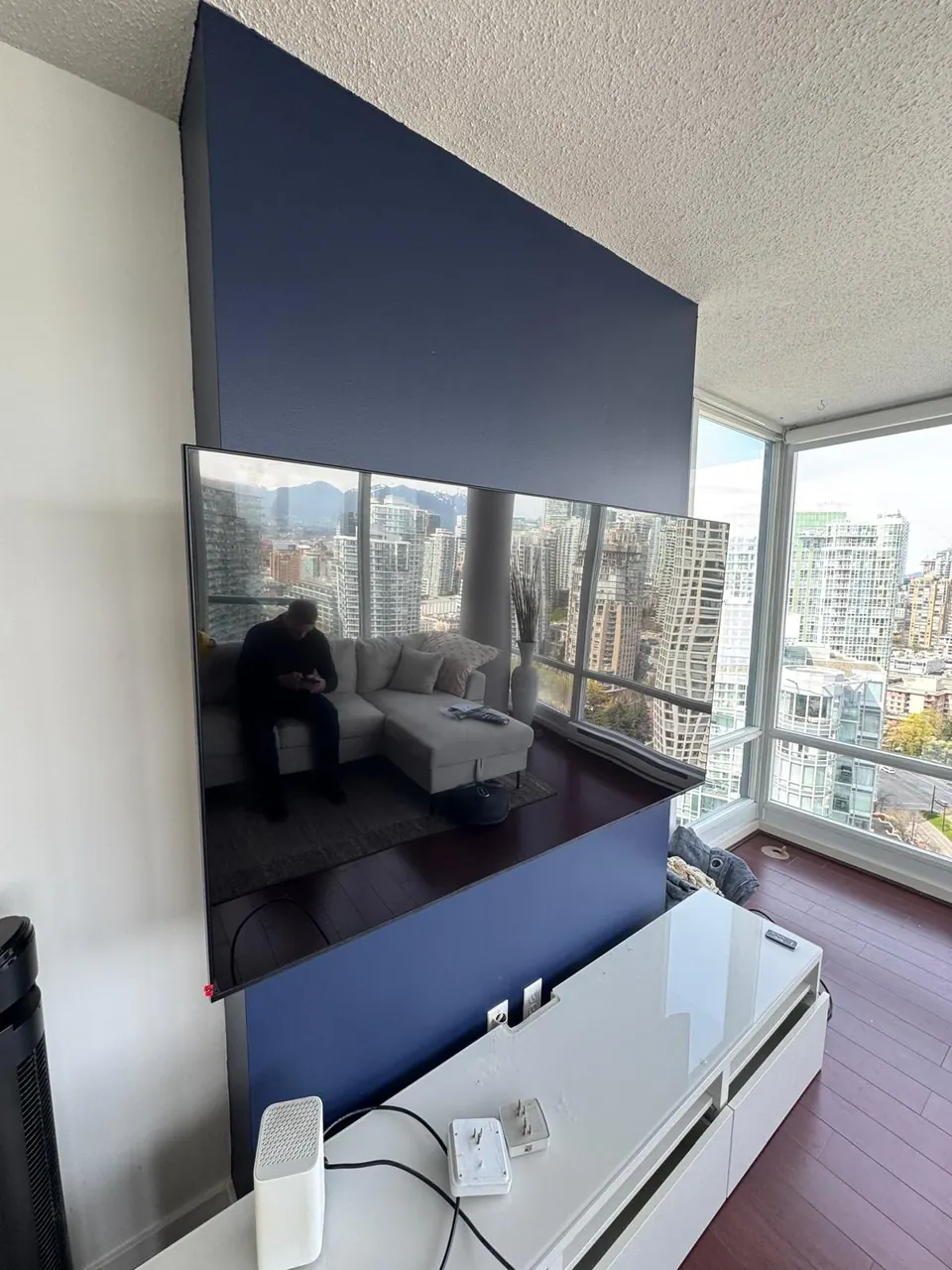 Completed: Large wall-mounted TV on a dark blue feature wall above a white media console